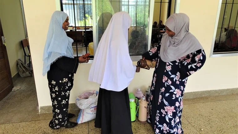 Two members of the study team distribute breakfast to a participant before treatment at Kilindi secondary school